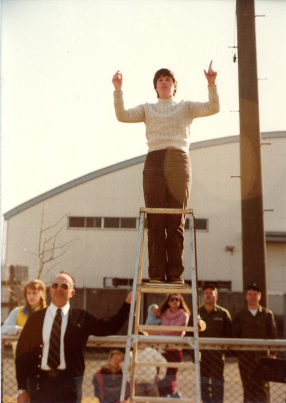 Band director leading on ladder as spectators look on from the sidelines