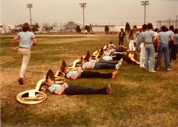 Band members laying down resting their heads inside bells of sousaphones