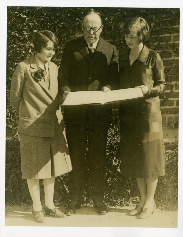 One man and two women looking at large book
