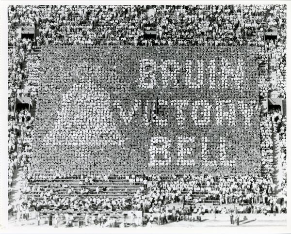 Crowd holds up cards that spell out "Bruin Victory Bell" and form a bell at football game, 1955