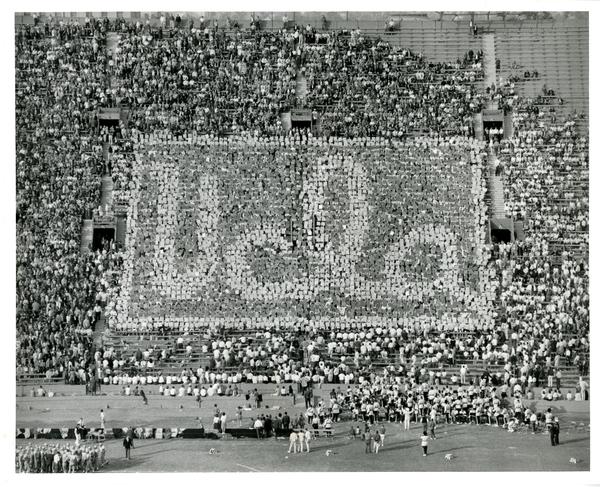 Crowd holds up cards that say UCLA at the football game, 1965