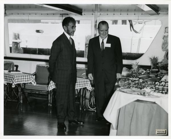Emperor Haile Selassie of Ethiopia and unidentified man look at food prepared for Emperor Selassie's visit on Motor Yacht Argo, April 25, 1967