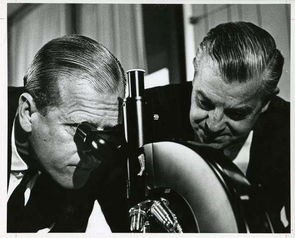 Prince Philip looks into a microscope with a UCLA professor