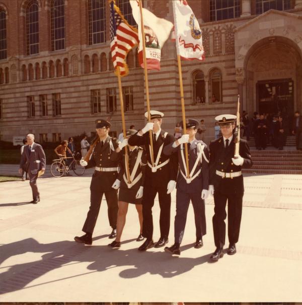 Color guard marching in front of Powell Library on Charter Day
