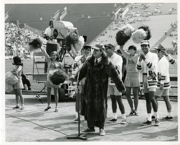 Student speaking to the crowd with UCLA cheerleaders during a football game