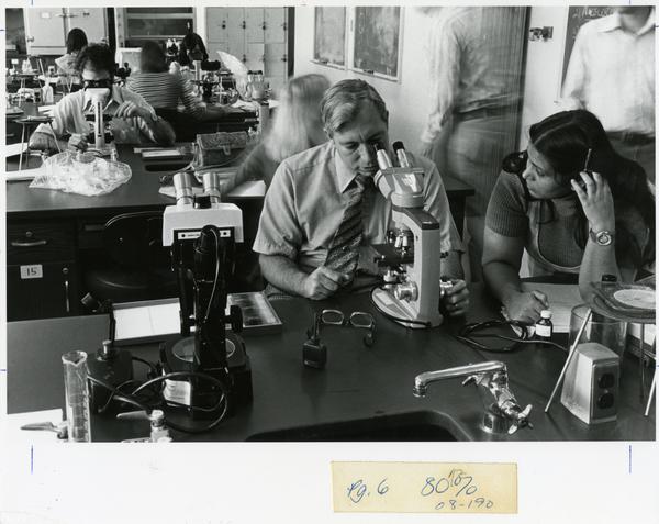 Student looks on as instructor looks through microscope, circa 1980's