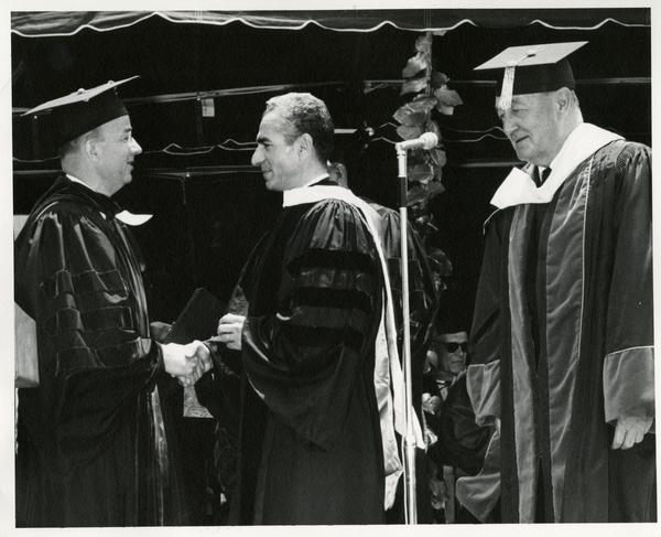 President Clark Kerr shaking hands with Mohammad Reza Pahlavi, the Shah of Iran, while Regent Edwin Pauley looks on at Commencement, 1964