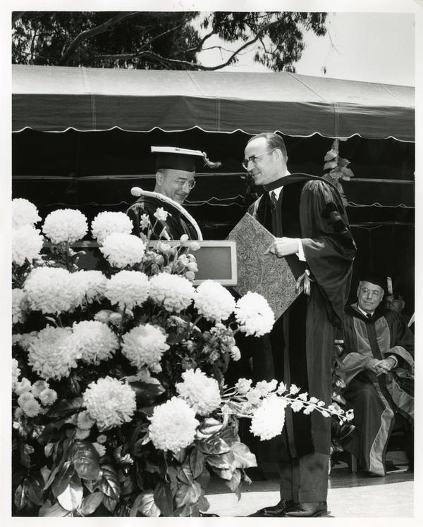 President Clark Kerr shaking hands with a unidentified man on stage at Commencement, 1964