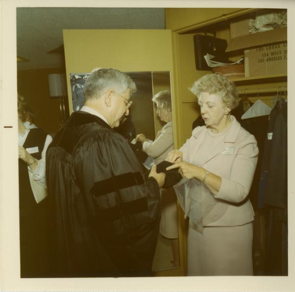 Woman assisting man with his hood at Commencement, June 17, 1970