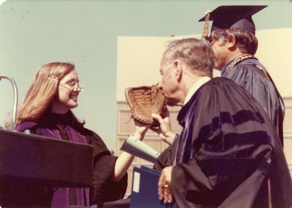 Darlene Walsh presents a baseball glove to Chancellor Young and Marshal Waldo Phelps at commencement, June 1976