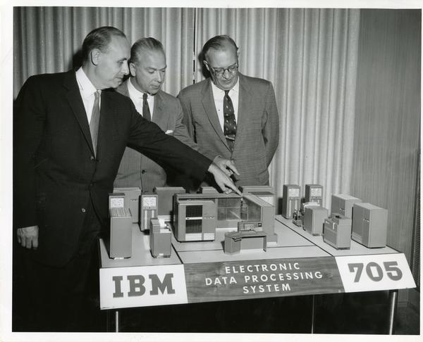 Dr. Cuthbert C. Hurd, Dean Neil Jacoby, and Chancellor Raymond B. Allen looking at a model of the IBM 705 computer for the Western Data Processing Center
