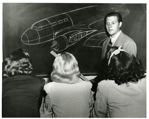 Teacher gesturing at plane drawn on blackboard