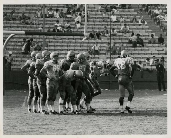 Football team gathered on the field during a game, ca. 1960s