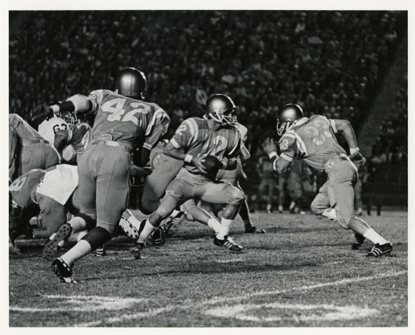 UCLA Quarterback Scott Henderson (12) prepares to hand off to Fullback Randy Tyler (33) with Flankerback Mike Cochran (42) coming around on the fake reverse against Oregon State.