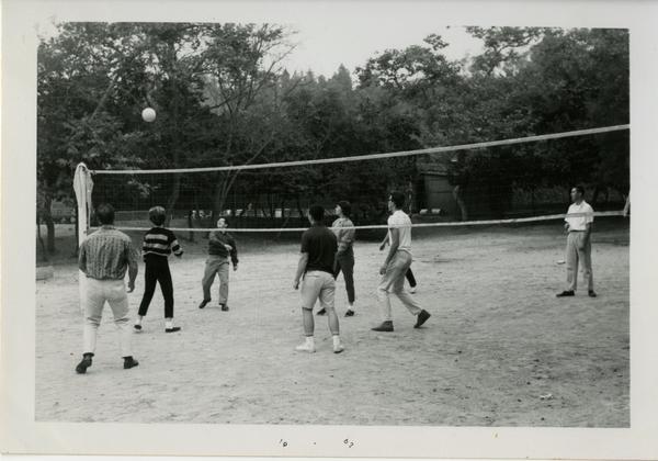 People, presumably of the geographic department, playing volleyball, possibly at the geography department picnic