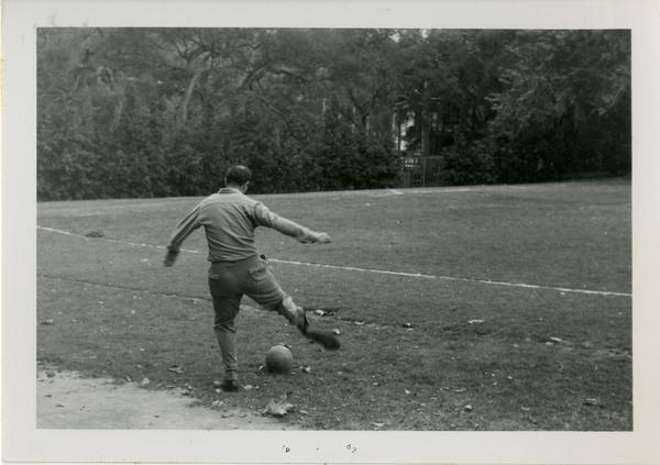 Man, possibly from the geography department, kicking a soccer ball