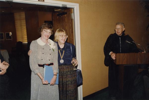 Victoria Fromkin hugs Beverly Liss with Raymond Fisher looking on from podium, June 1988