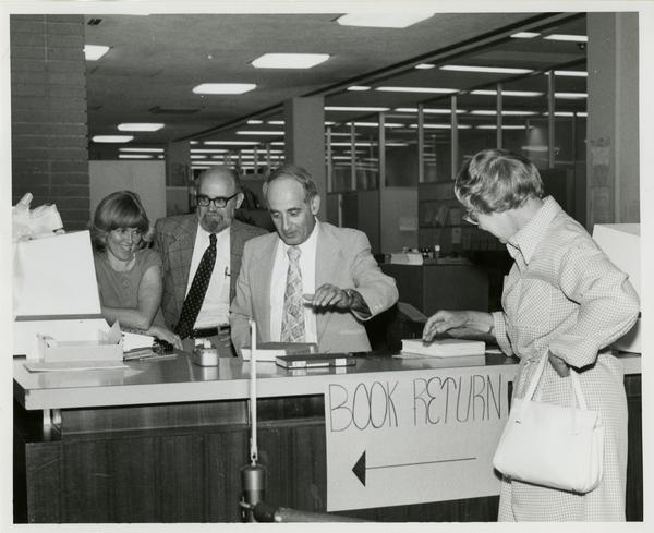 Linda Fierro, Jim Cox, and Russell Shank stand behind desk as Page Ackerman walks up
