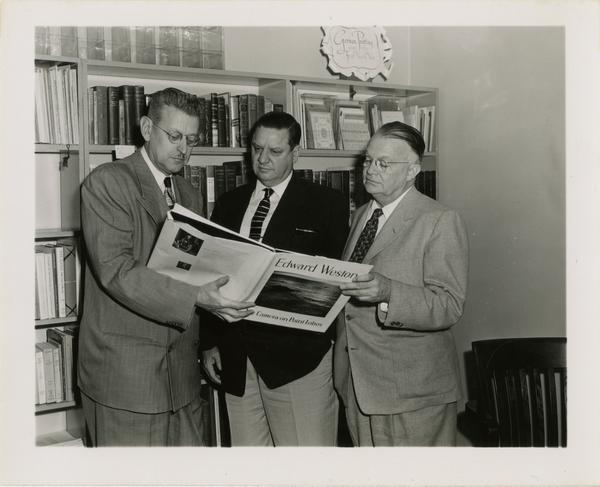 Three men looking photography book by Edward Weston, ca. 1953