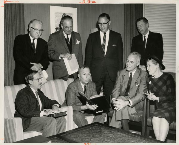 The UCLA Library's two millionth book is examined by Chancellor Franklin D. Murphy at the 1964 presentation ceremony as Robert Vosper, Regent Edward W. Carter, Mrs. Elmer Belt, Dr. Elmer Belt, Prof. Majl Ewing, W. Thomas Davis, Prof. C.D.O'Malley sit and stand beside him.