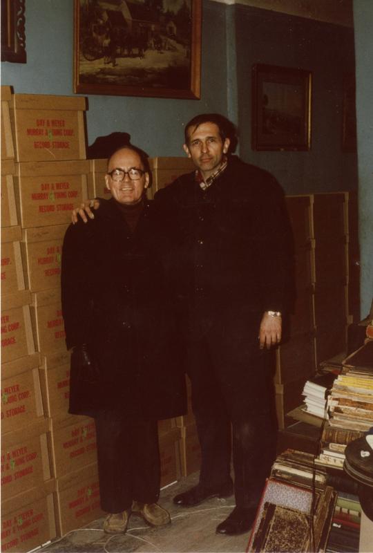 Two men standing beside boxes in Music Library at Schoenberg Hall