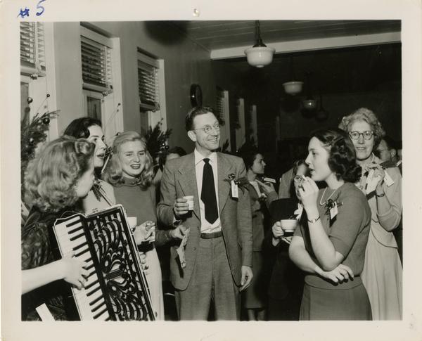 Neil Harlow stands in middle of group of library staff while woman plays accordian at Library Christmas party
