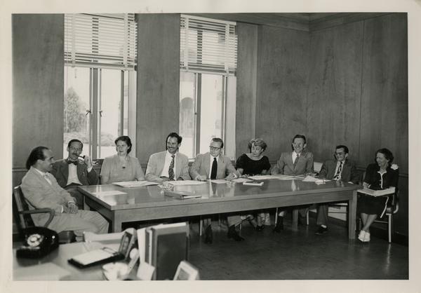 Lawrence Clark Powell sitting at end of table speaking to colleagues