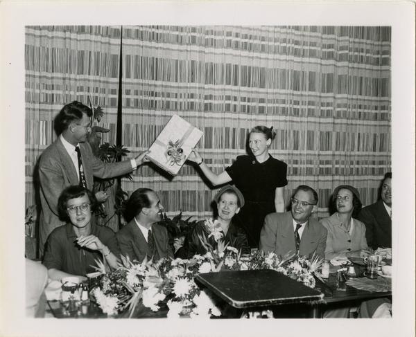 Page Ackerman, Lawrence Clark Powell, Mrs. Elmer Belt, and Chancellor Allen sitting as two other staff exhange gift at Library staff Christmas party, December 19, 1957