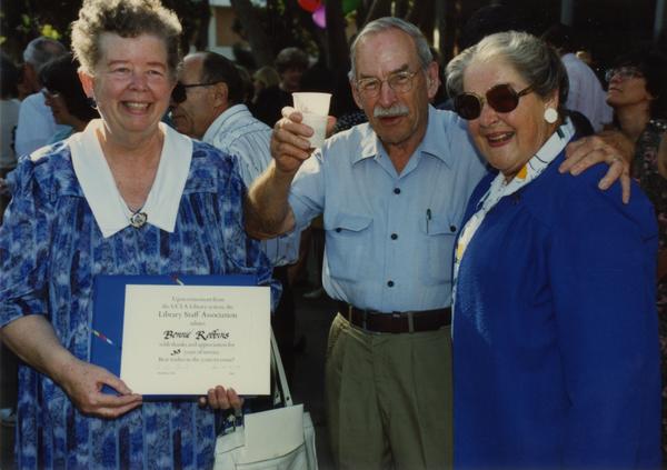 Library staff holds up her certificate while other staff members cheer and smile for the camera, ca. 1991