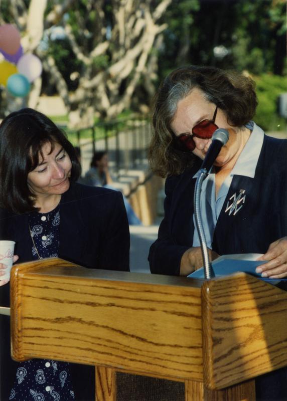 Speaker flips through a folder at the podium at the staff retirement party, 1991