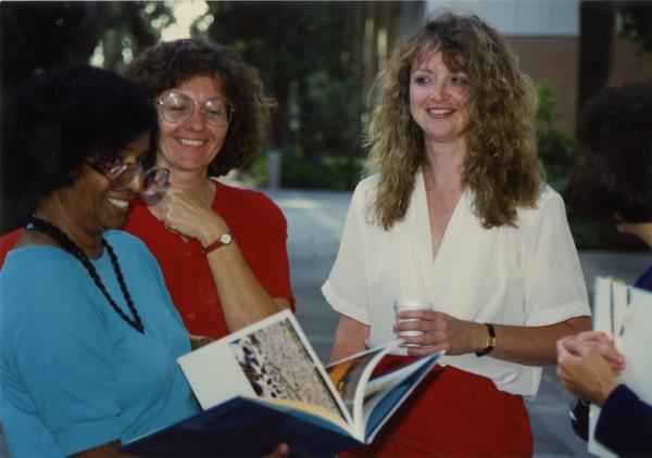 Library staff look on as another staff member looks through a book at the staff retirement party, 1991