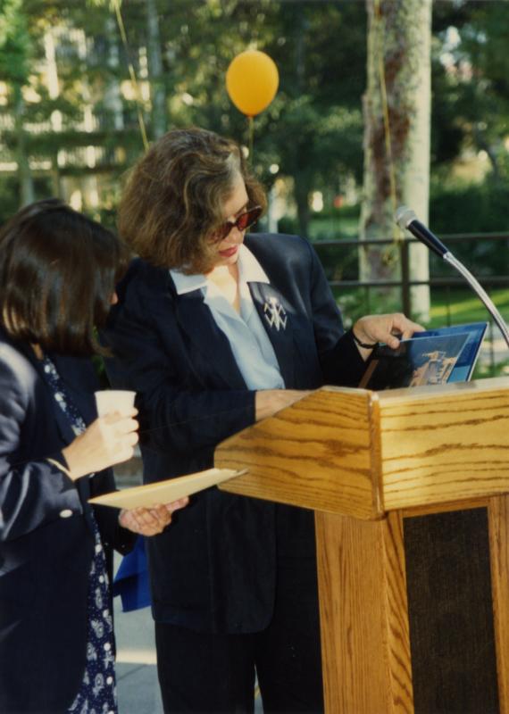 Woman flips through a book at the podium as another staff worker looks on, 1991