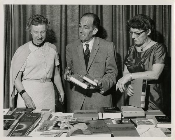Lawrence Clark Powell and two unidentified UCLA library personell peruse through books laid out on a table during a visit to Japan, ca. 1960
