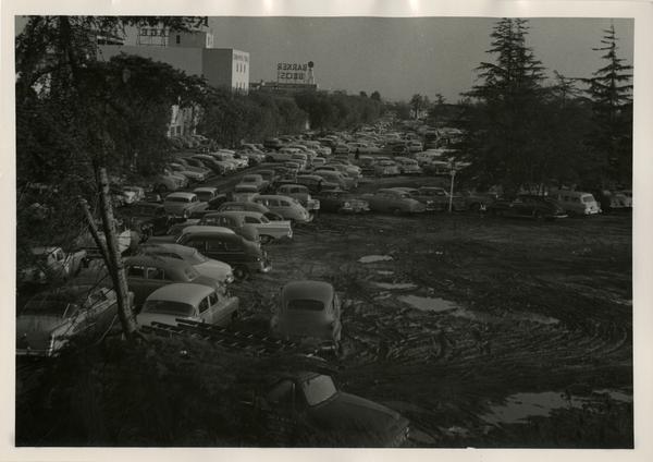 Cars parked on a dirt lot with Barker Bros sign in background
