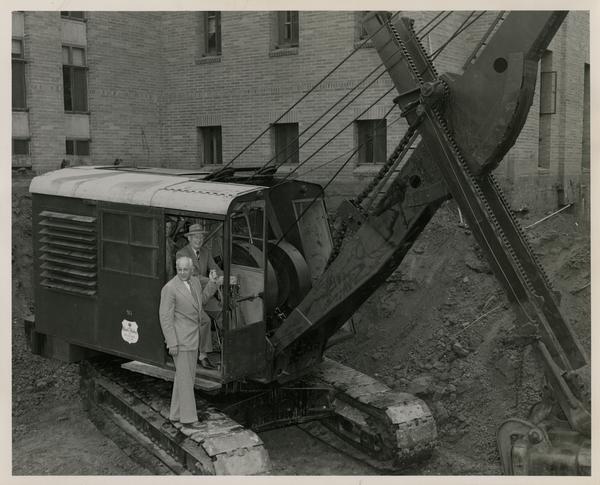 Two men posing by excavator scoop in construction area beside Powell Library, June 24, 1947