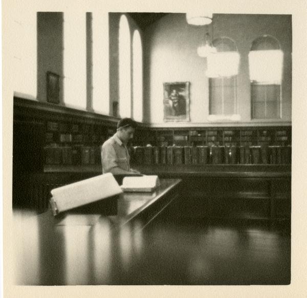 Looking towards the northeast corner of the Main Reading Room at Powell Library with a man standing at reference desk, 1949