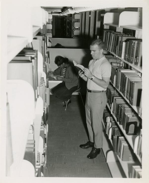 Student checking out a book in the Powell Library stacks