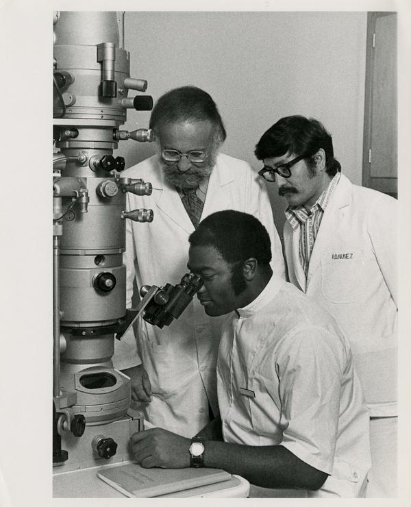 Three scientists using large microscope in School of Public Health laboratory