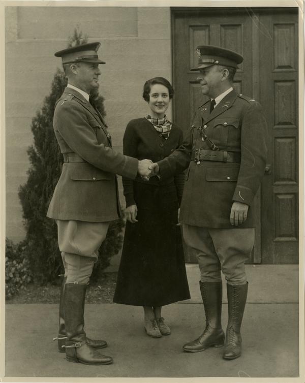 Photo of two men in uniform shaking hands while woman stands in center smiling