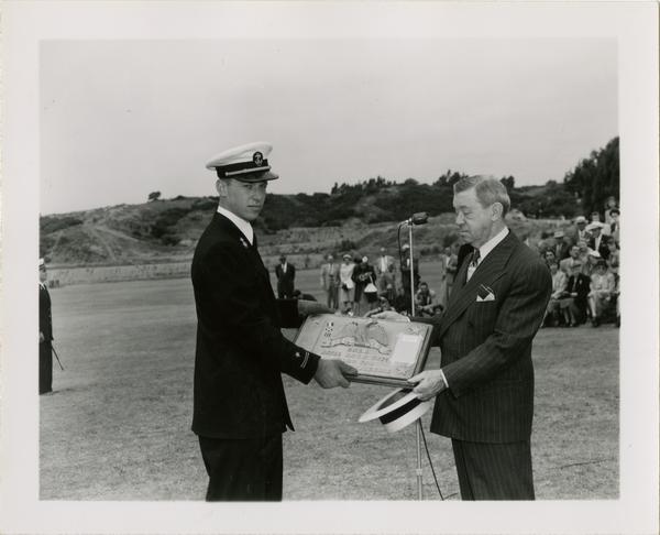 Naval officer and civilian holding award of excellence plaque