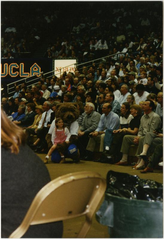 Girl sitting on Joe Bruin's lap at basketball game, ca. February 1997