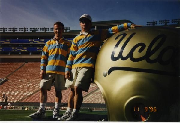 Members of Spirit Squad posing on field by a large UCLA football helmet, ca. 1996