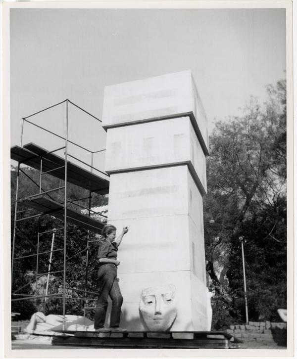 Anna Mahler standing beside fifteen foot limestone column with clay model sketch before sculpting