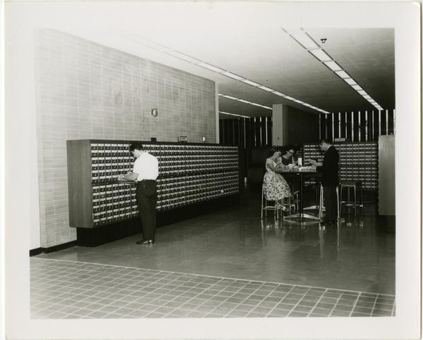 One student looks through the card catalog while other students study at a table in the University Research Library