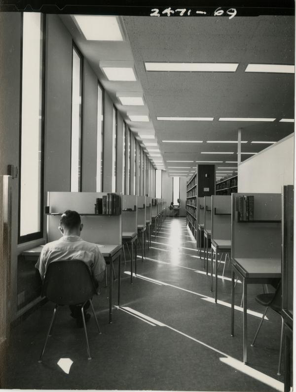 Students studying at desks along the stacks in the University Research Library, ca. 1964