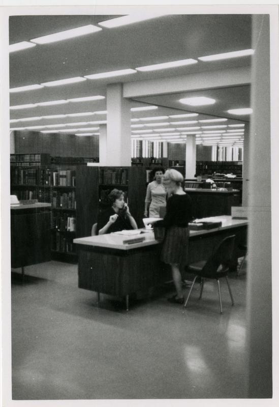 Part of the reference staff sitting at reference desks in a room of the University Research Library, ca. 1968