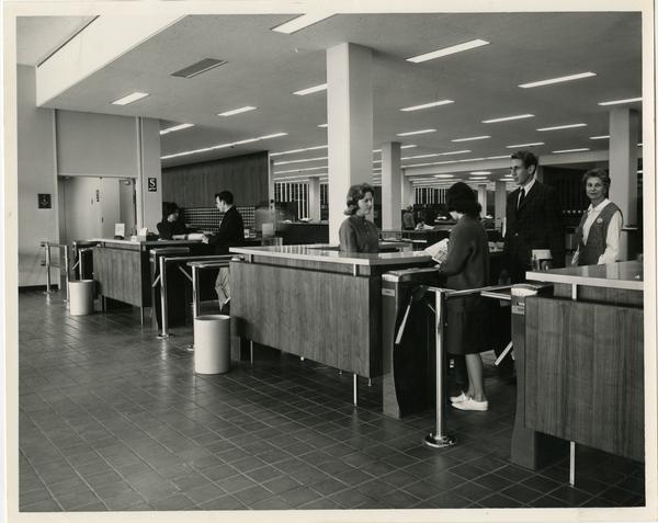 Students waiting in line to talk to library staff workers before exiting the University Resarch Library, ca. 1964