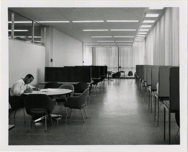 View of student working at table in University Research Library surrounded by study cubicles