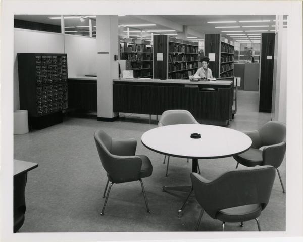 Library employee seated behind desk, ca. 1964