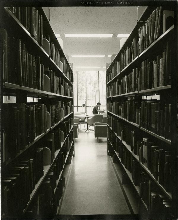 Contact print of student sitting at desk at the end of stacks, ca. 1964